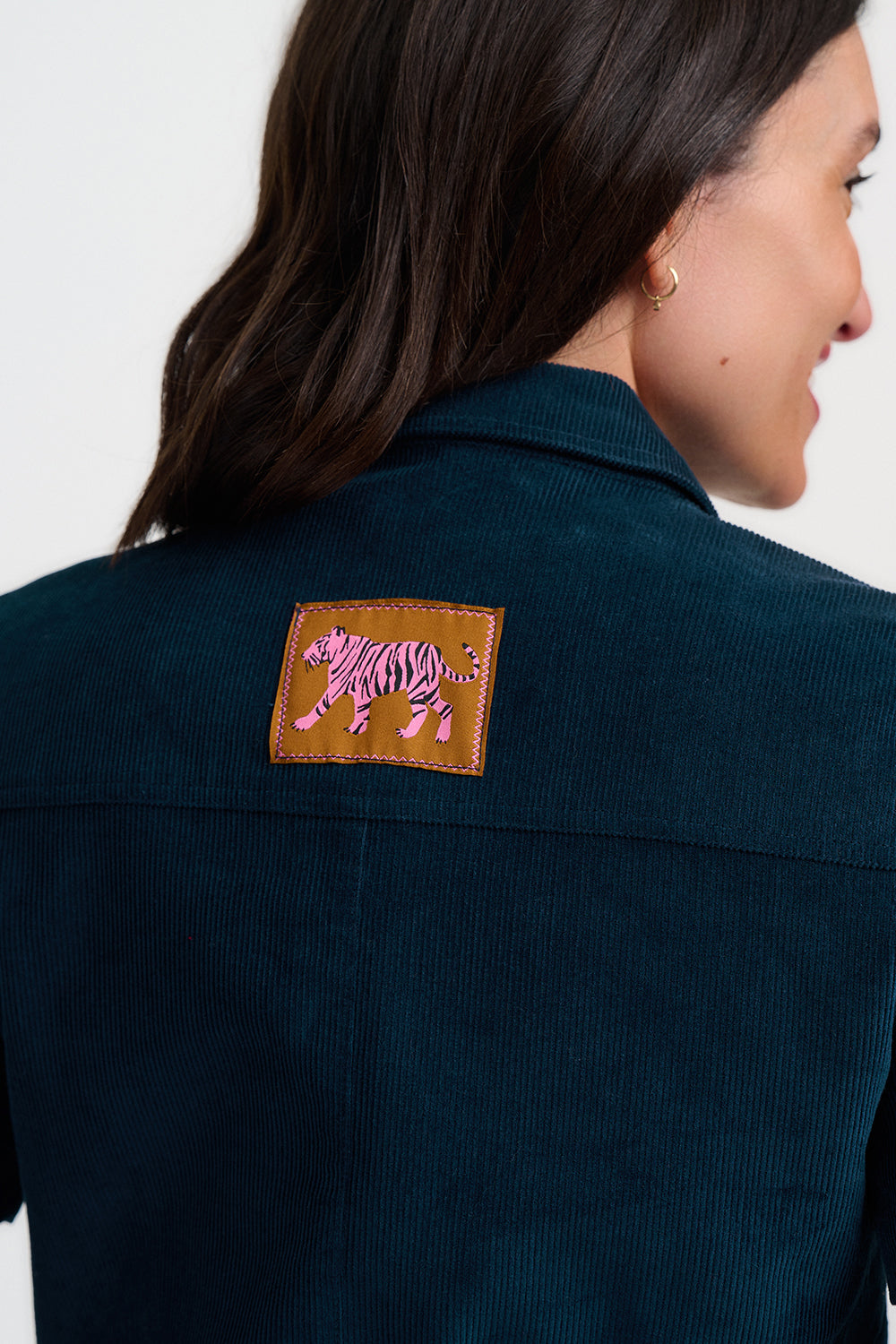 Close-up back view of a woman wearing a dark navy corduroy jacket, featuring a brown leather patch on the upper back with a pink and black zebra design.