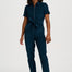 A woman modeling a dark teal short-sleeve jumpsuit with a front zipper and matching waist tie, paired with brown and white sneakers, against a plain white studio background.
