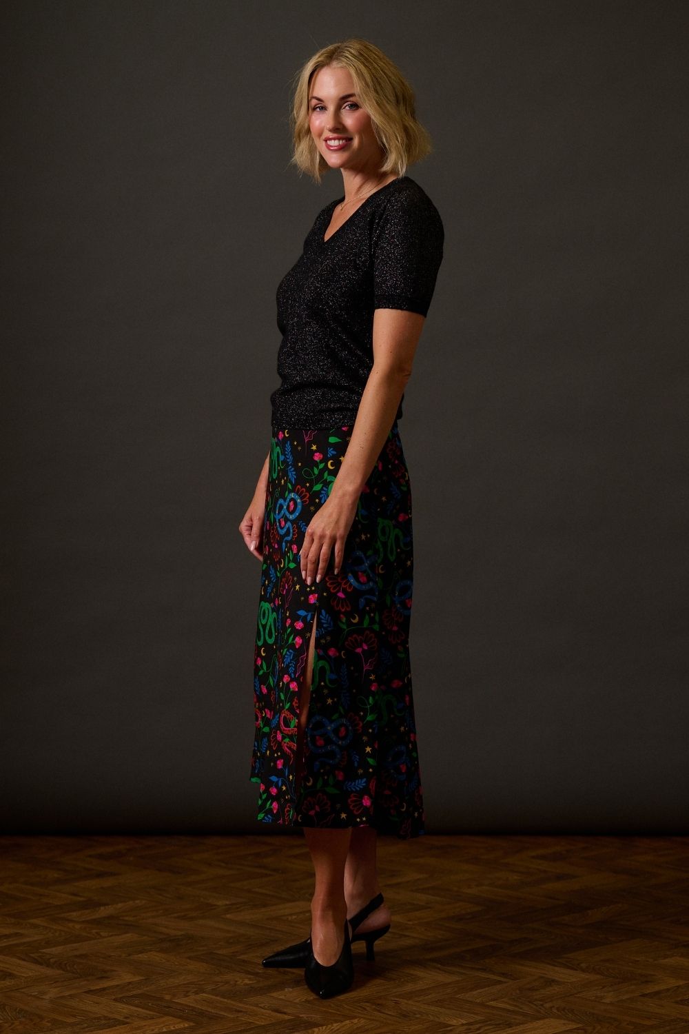 Woman wearing a black top and colorful patterned skirt against a dark background