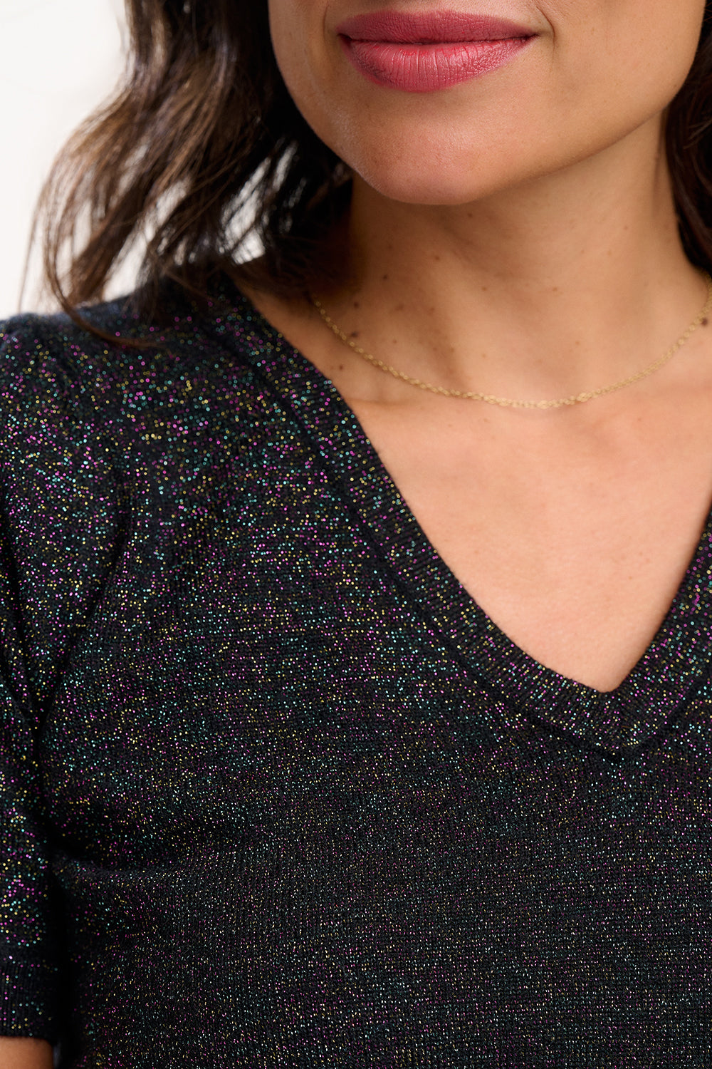 Close-up of a person wearing a black glittery top with a V-neckline.