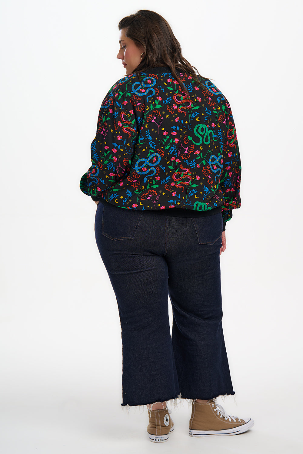 Person wearing a colorful patterned jacket and dark jeans on a white background