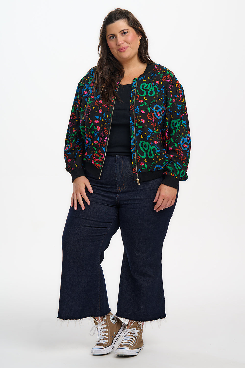 Woman wearing a colorful jacket, black top, and dark jeans on a white background