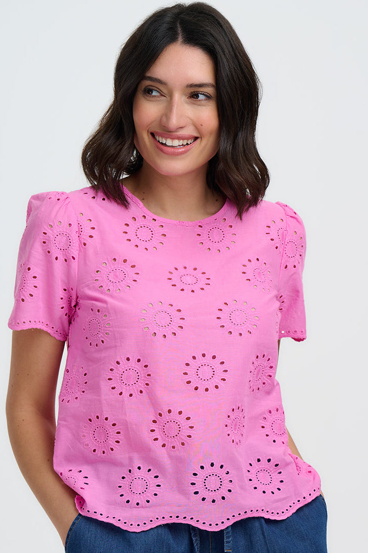 Woman wearing a pink top with cut-out patterns and blue shorts on a white background