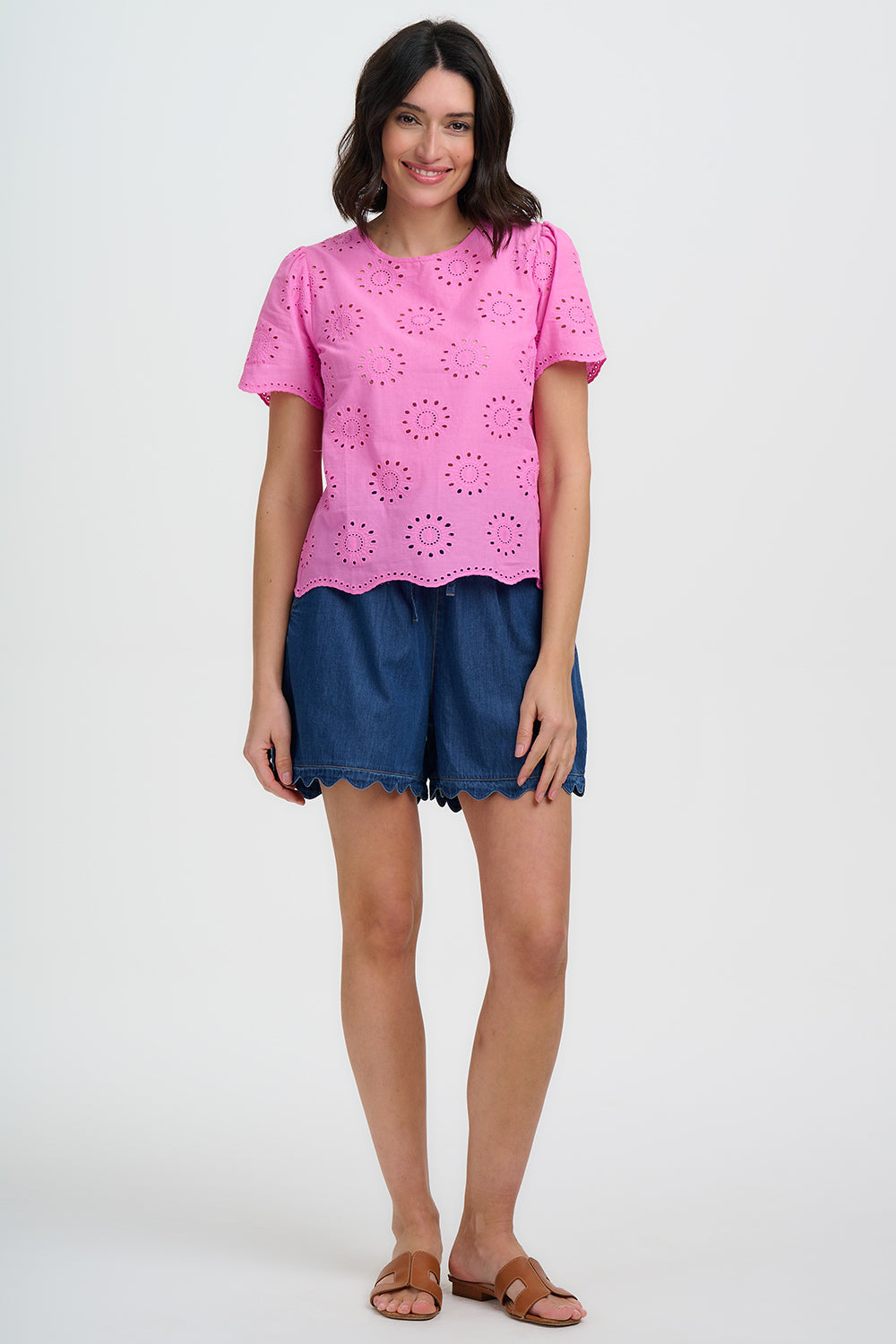 Woman wearing a pink top with cut-out patterns and blue shorts on a white background