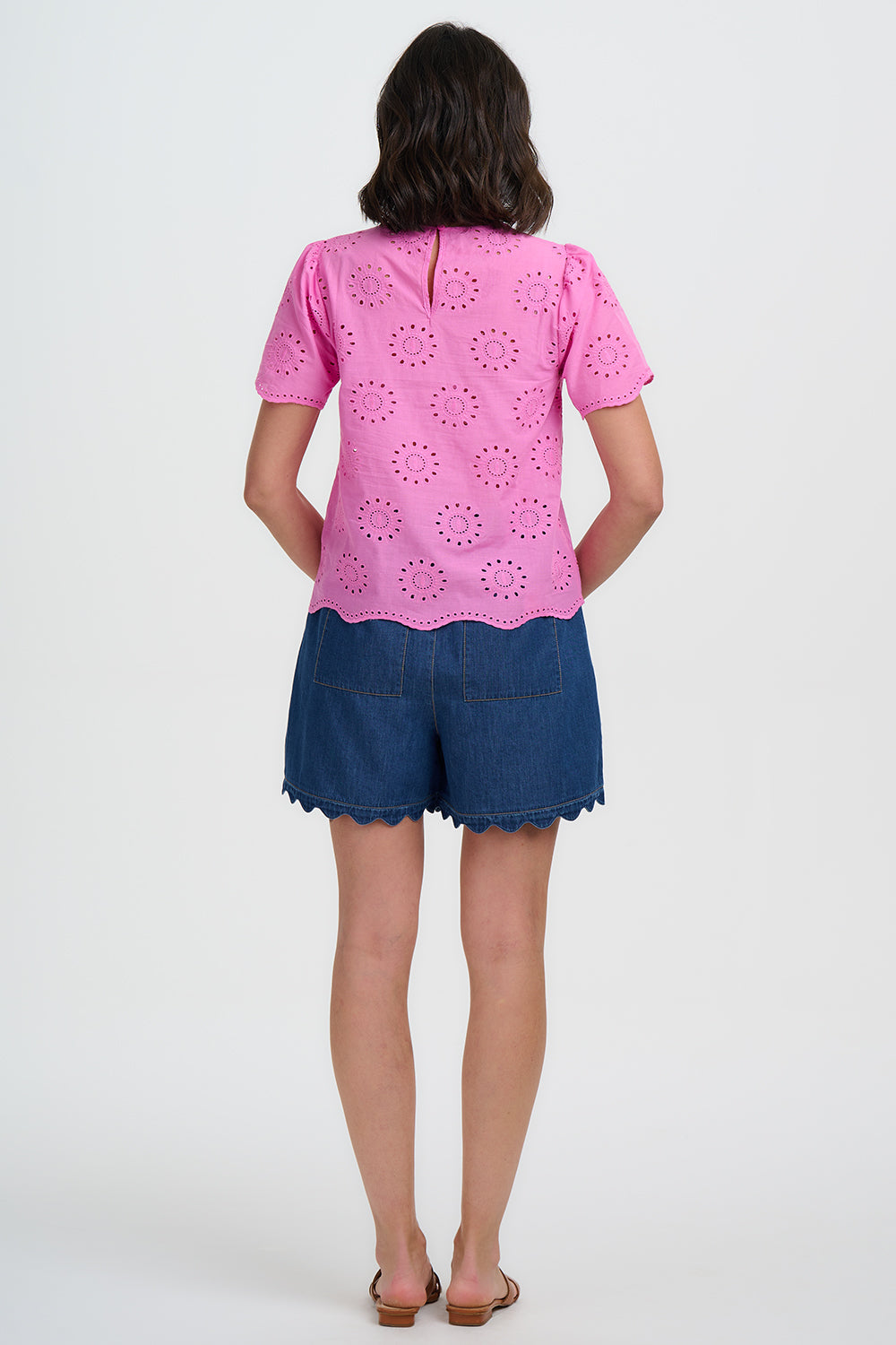 Person wearing a pink top with cut-out patterns and blue denim shorts on a white background