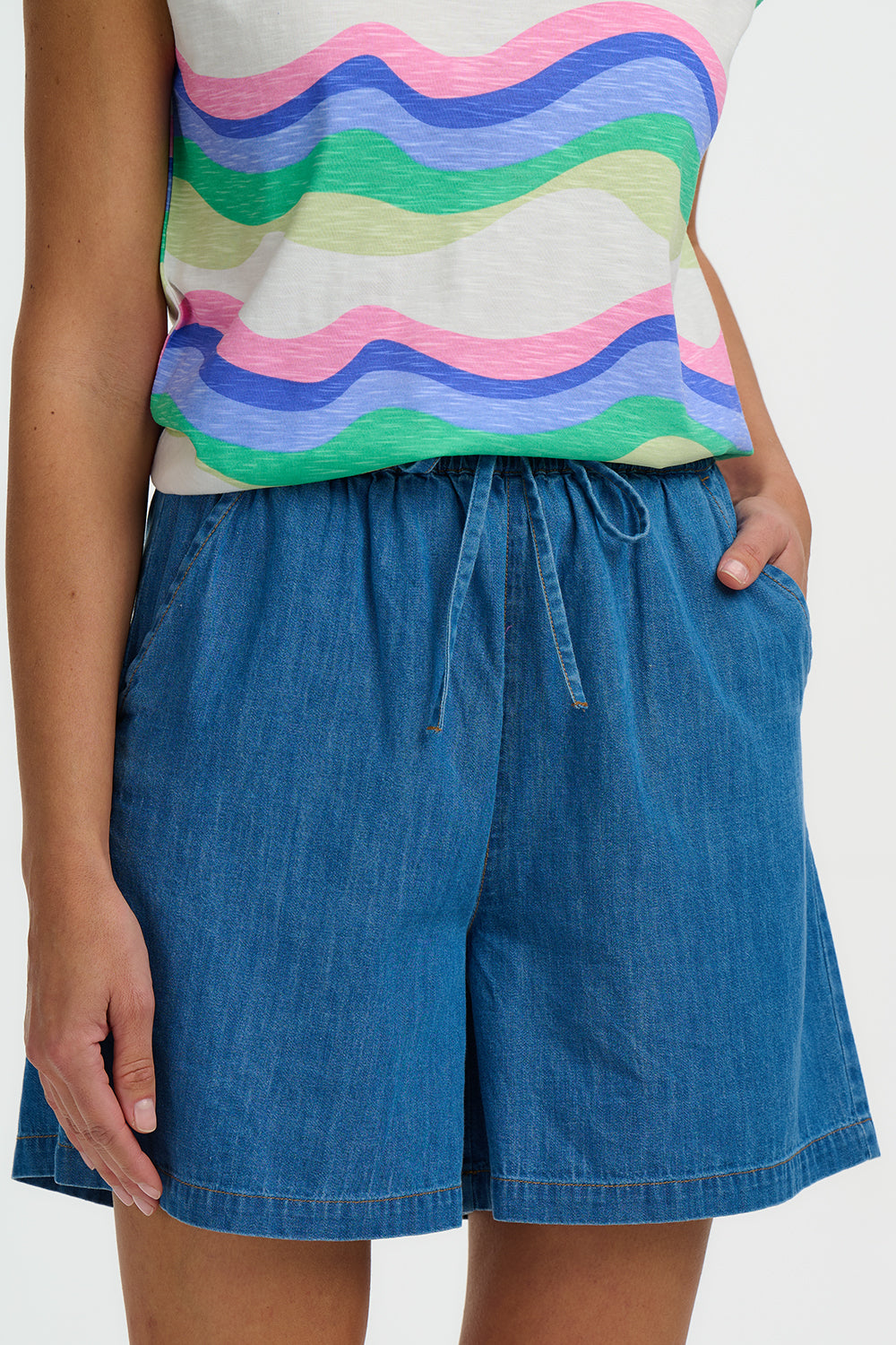 Person wearing a colorful striped top and blue denim shorts on a white background
