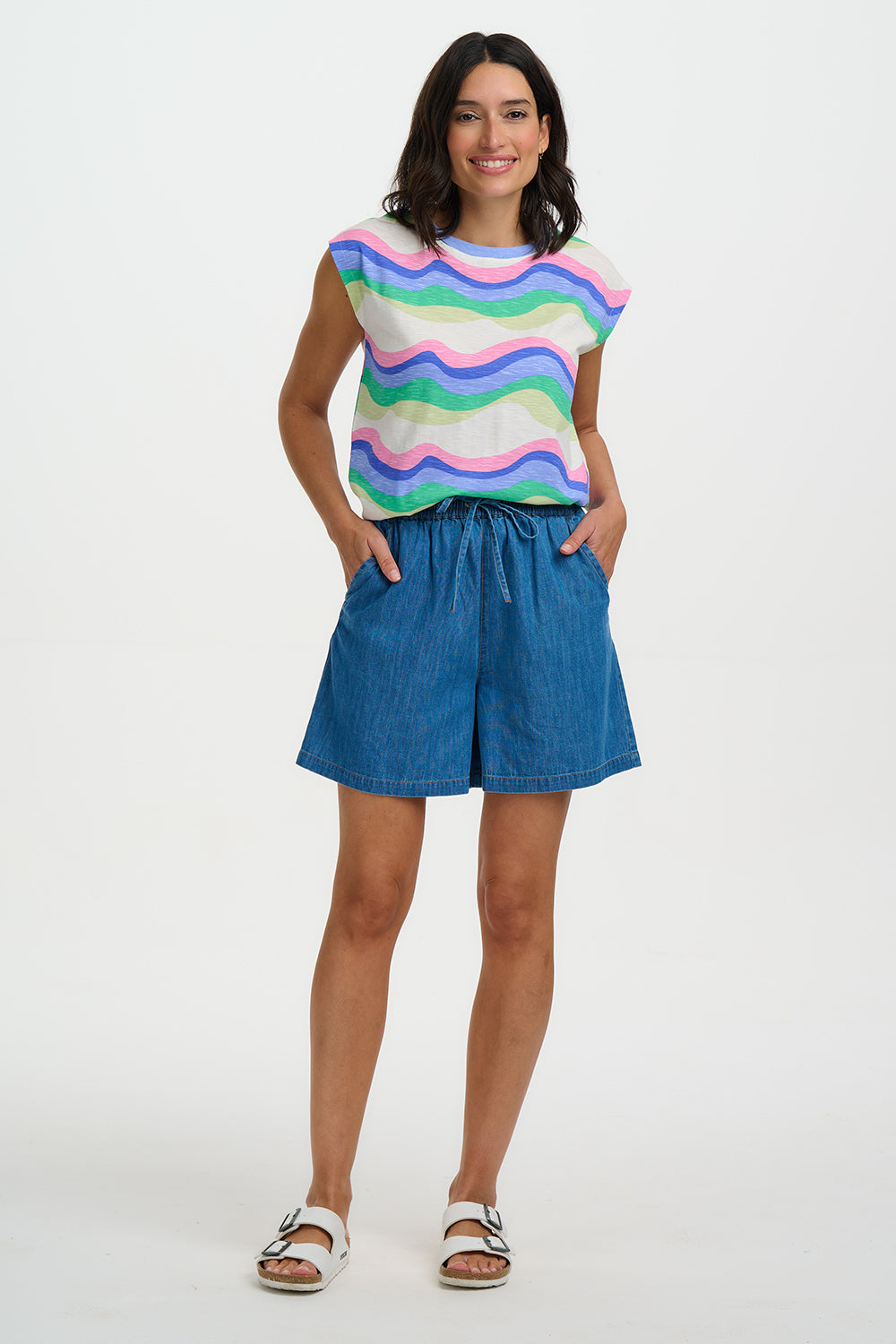 Woman wearing a colorful striped shirt and blue shorts on a white background
