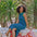 Woman in a blue dress sitting on a mosaic bench with green plants in the background