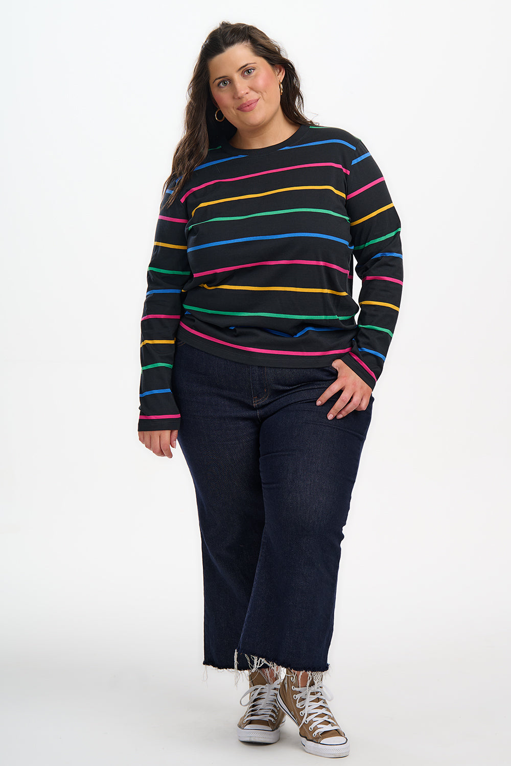 Person wearing a black sweater with colorful stripes and dark jeans on a white background