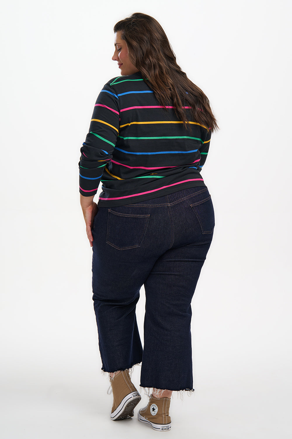Person wearing a colorful striped shirt and dark jeans on a white background