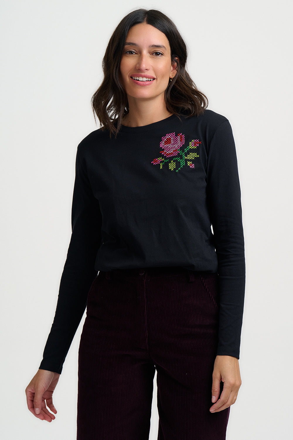 Woman wearing a black long-sleeve shirt with a floral embroidery design on a white background