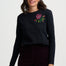 Woman wearing a black long-sleeve shirt with a floral embroidery design on a white background