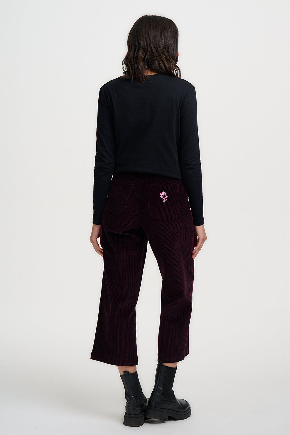 Person wearing a black long-sleeve top and maroon pants on a white background
