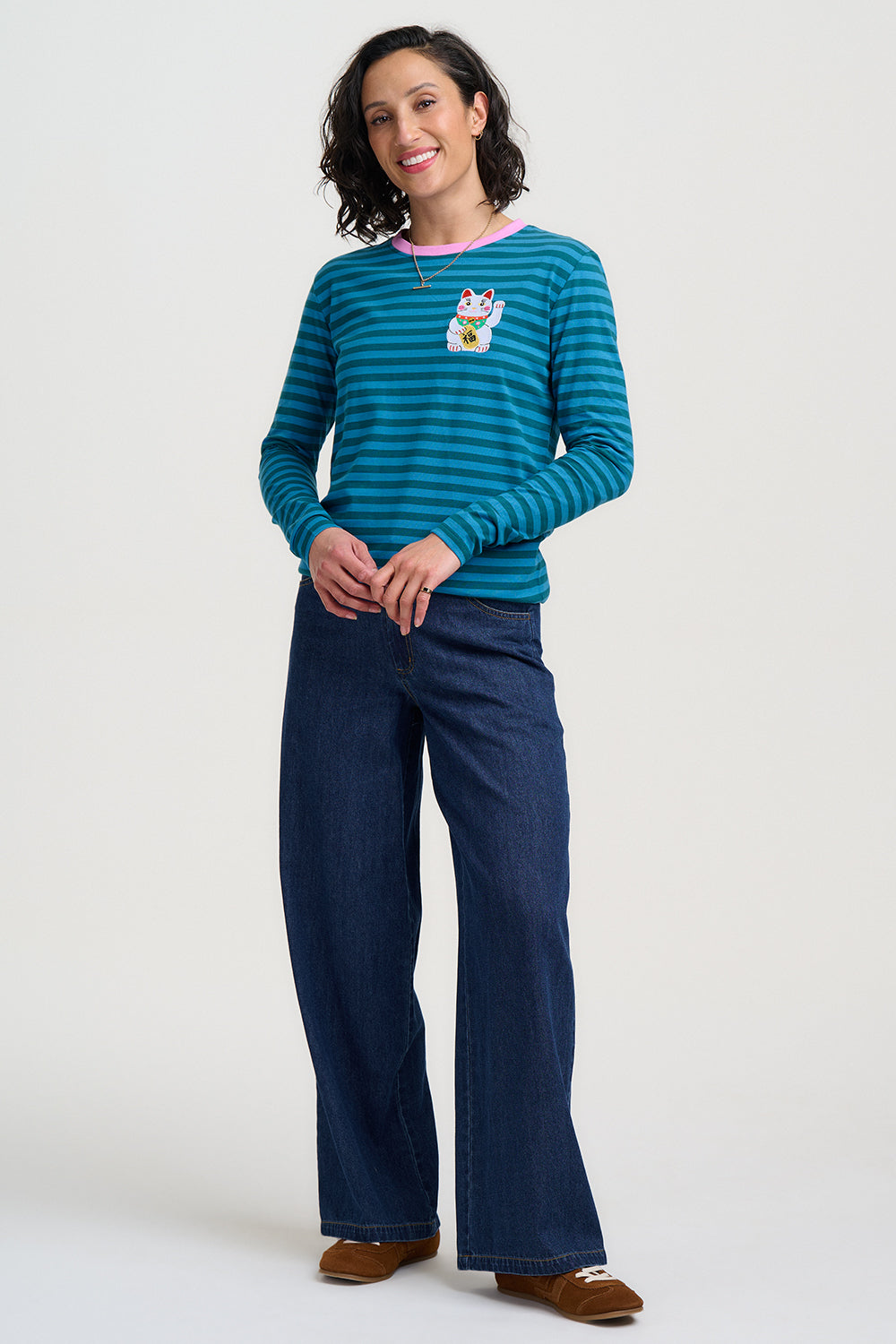 Woman wearing a blue striped sweater with a cartoon character and dark blue pants on a white background