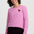 A woman wearing a pink and white striped long-sleeve shirt with a small embroidered chicken on the left chest, paired with dark burgundy pants, against a light gray studio background.