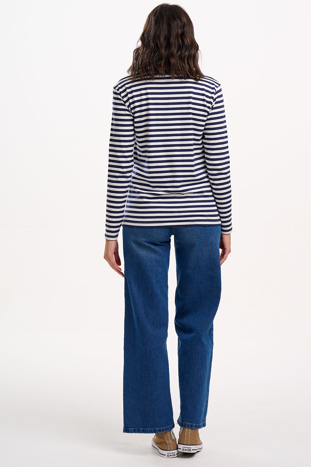Person wearing a striped shirt and blue jeans on a white background