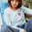 Woman wearing a light blue and white striped long-sleeve shirt with a heart design, sitting on a blue chair.
