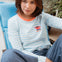 Woman wearing a light blue and white striped long-sleeve shirt with a heart design, sitting on a blue chair.