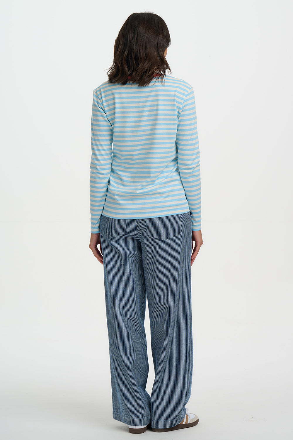 Person wearing a striped long-sleeve top and blue pants on a white background