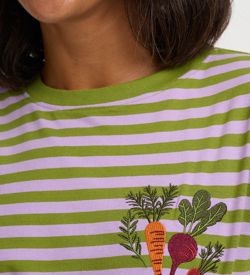 Close-up of a person wearing a green and light pink striped t-shirt with an embroidered vegetable motif on the chest.