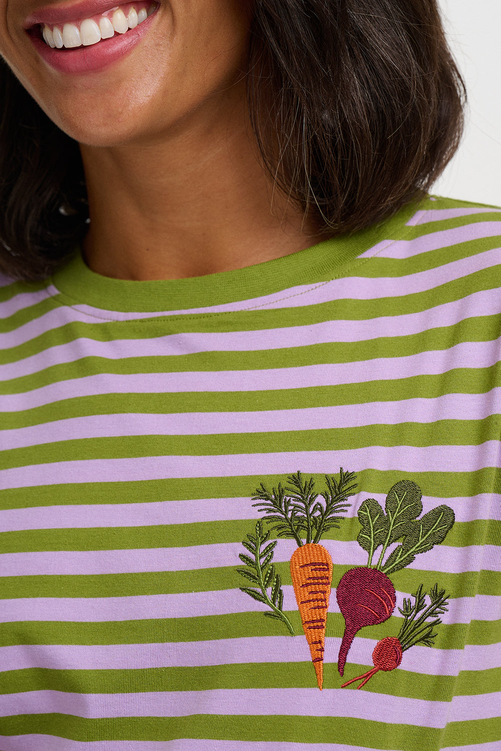 Close-up of a person wearing a green and light pink striped t-shirt with an embroidered vegetable motif on the chest.