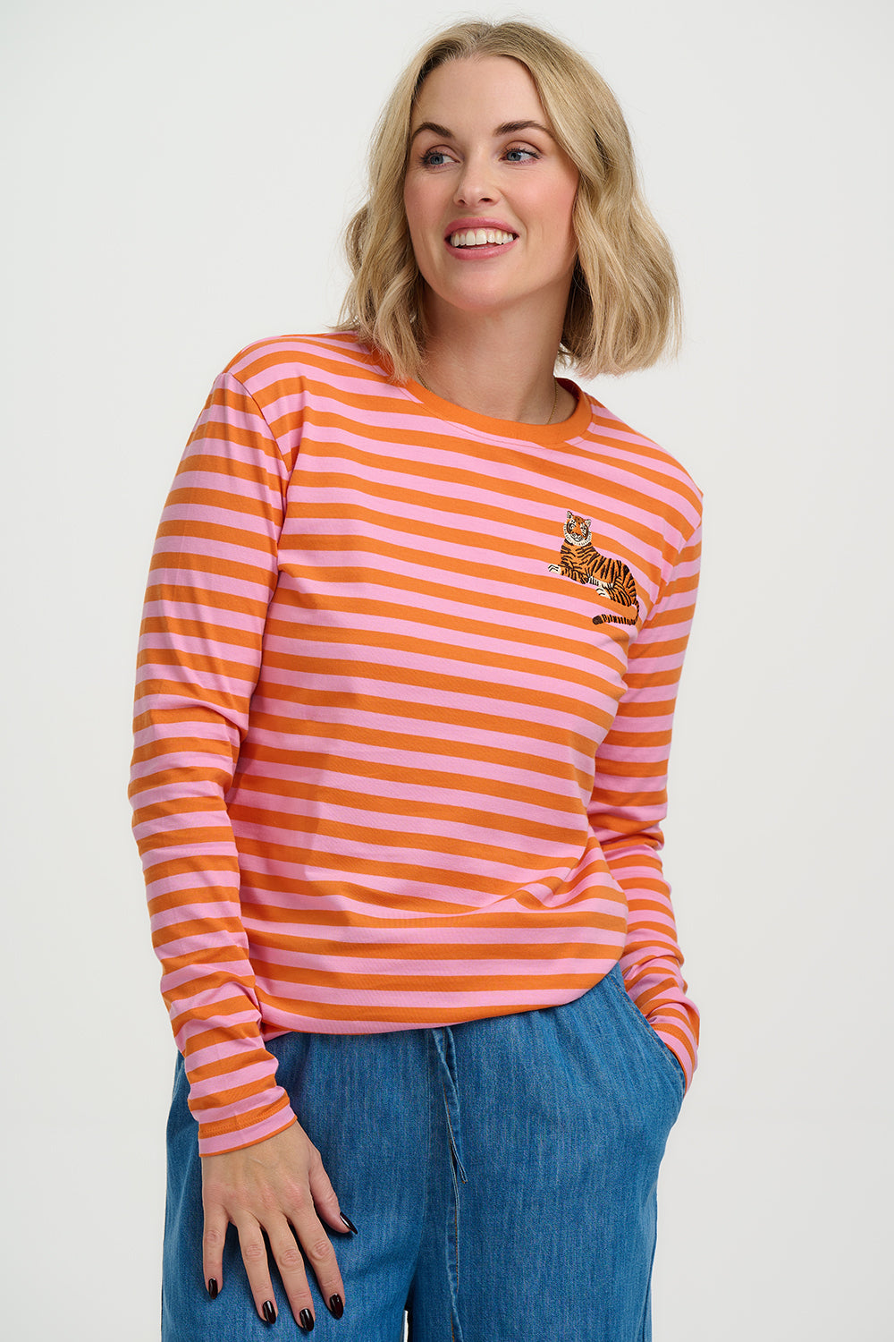Woman wearing an orange and pink striped long-sleeve shirt with a small logo on a white background