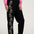 Person wearing black pants with floral embroidery and a pink sweatshirt on a white background