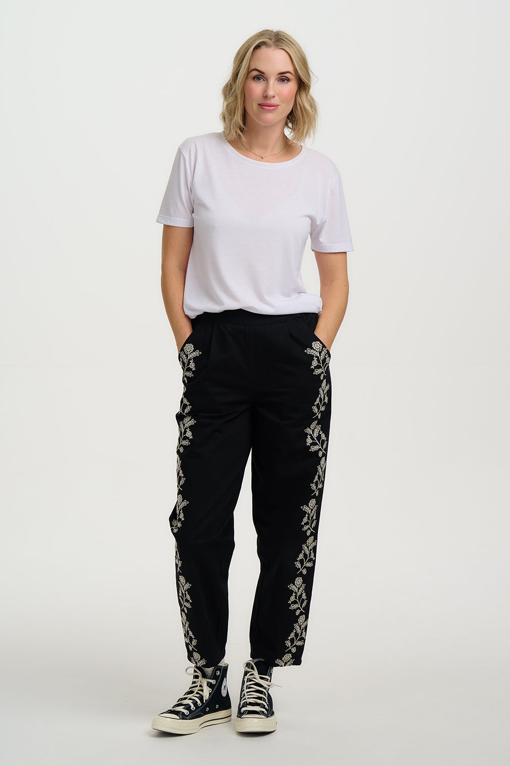 Woman wearing a white t-shirt and black pants with floral embroidery on a white background