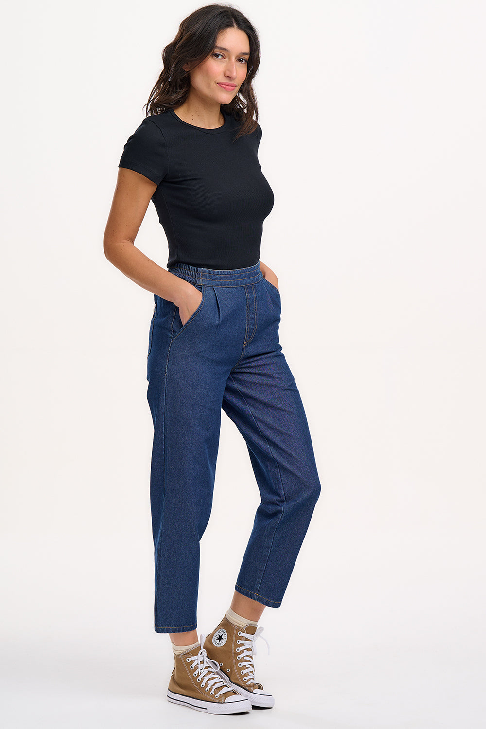 A model wearing the Calista Trousers in deep blue denim with a black top, showcasing the side and front pockets.