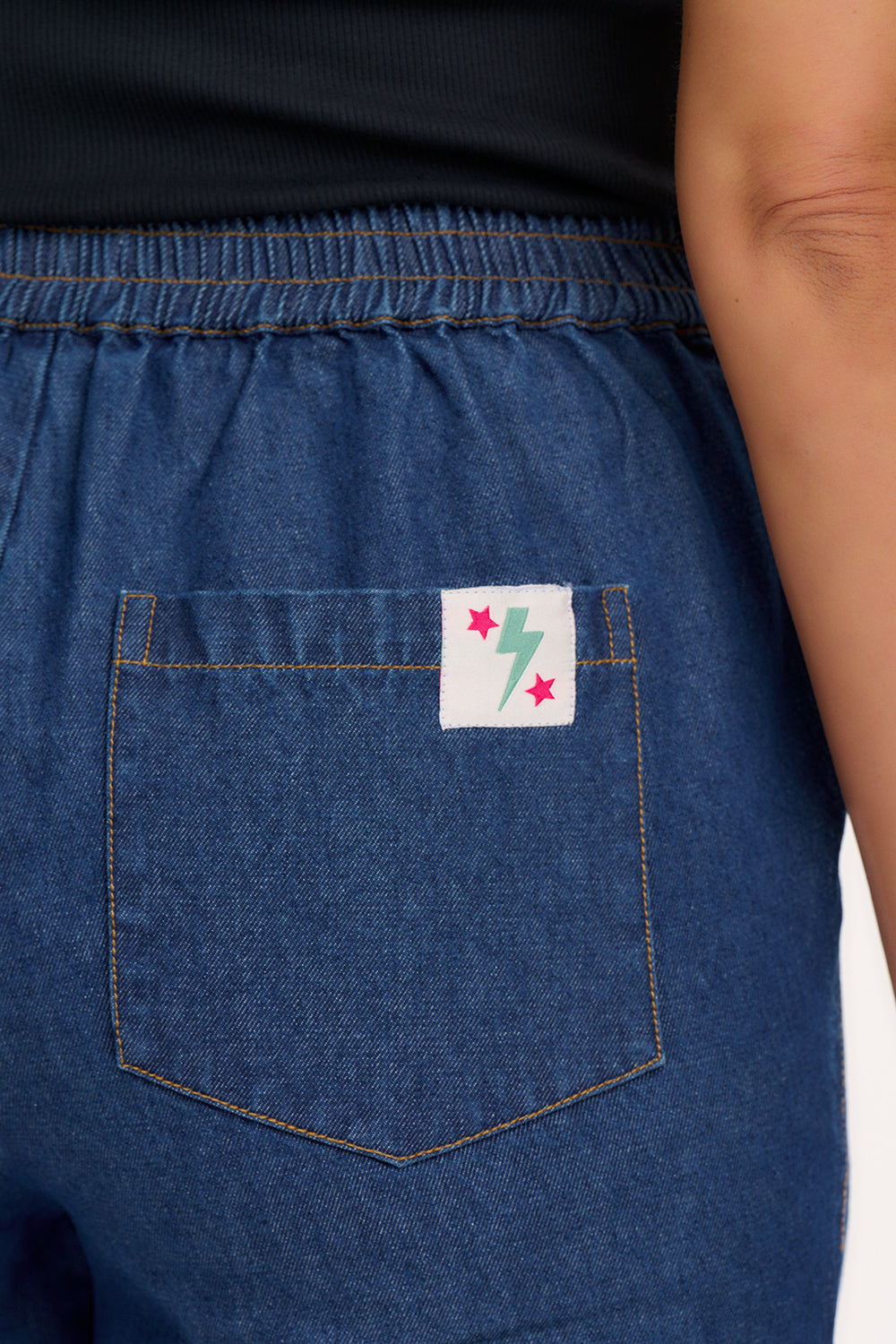 A model wearing the Calista Trousers in deep blue denim with a black top, showcasing the side and front pockets.