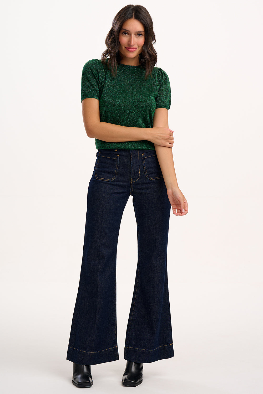 Woman wearing a green top and dark blue jeans on a white background