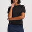 A woman modeling a short-sleeve dark gray knit top and a dark blue denim mini skirt with a scalloped hem, against a light gray studio background.