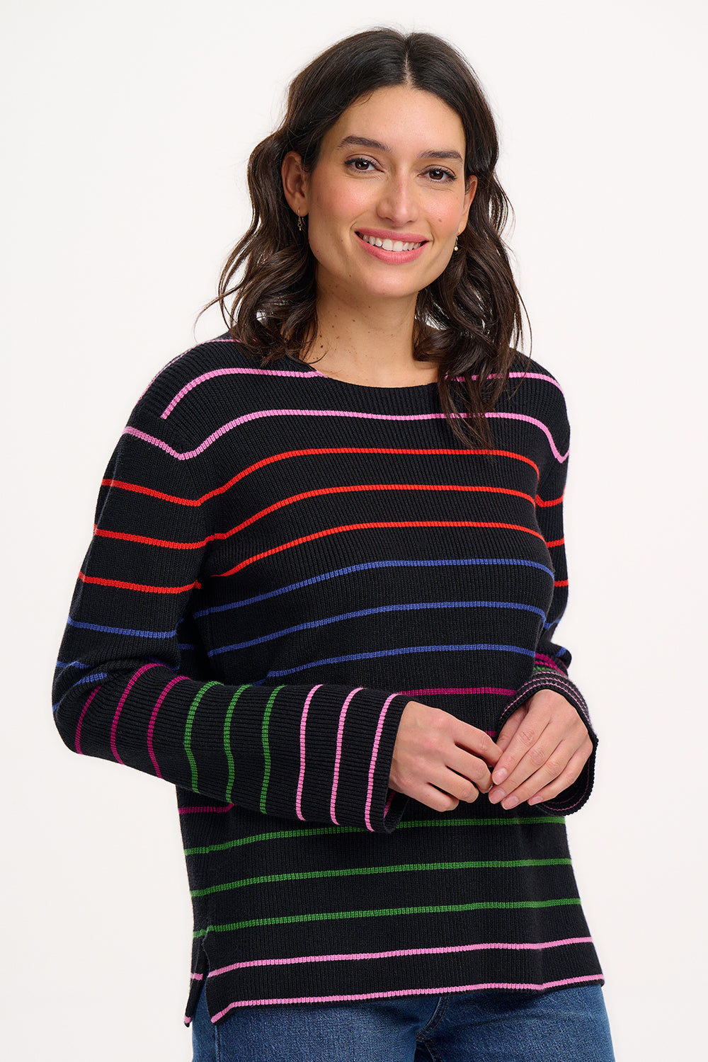 A woman wearing a black long-sleeved jumper with horizontal rainbow stripes in pink, red, blue, and green.