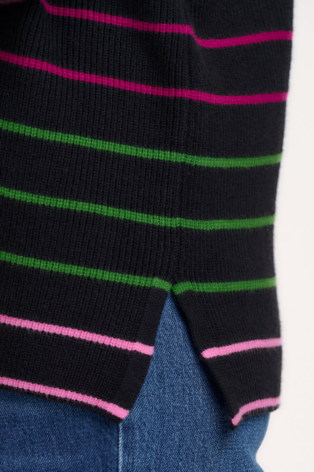 A woman wearing a black long-sleeved jumper with horizontal rainbow stripes in pink, red, blue, and green.