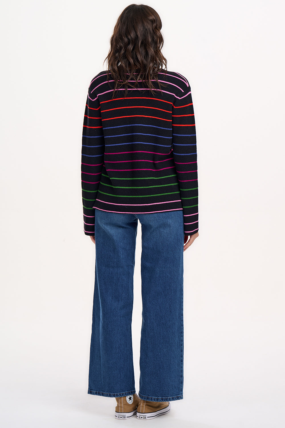 A woman wearing a black long-sleeved jumper with horizontal rainbow stripes in pink, red, blue, and green.
