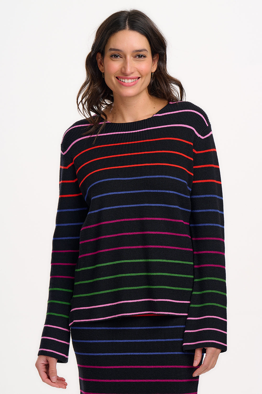 A woman wearing a black long-sleeved jumper with horizontal rainbow stripes in pink, red, blue, and green.