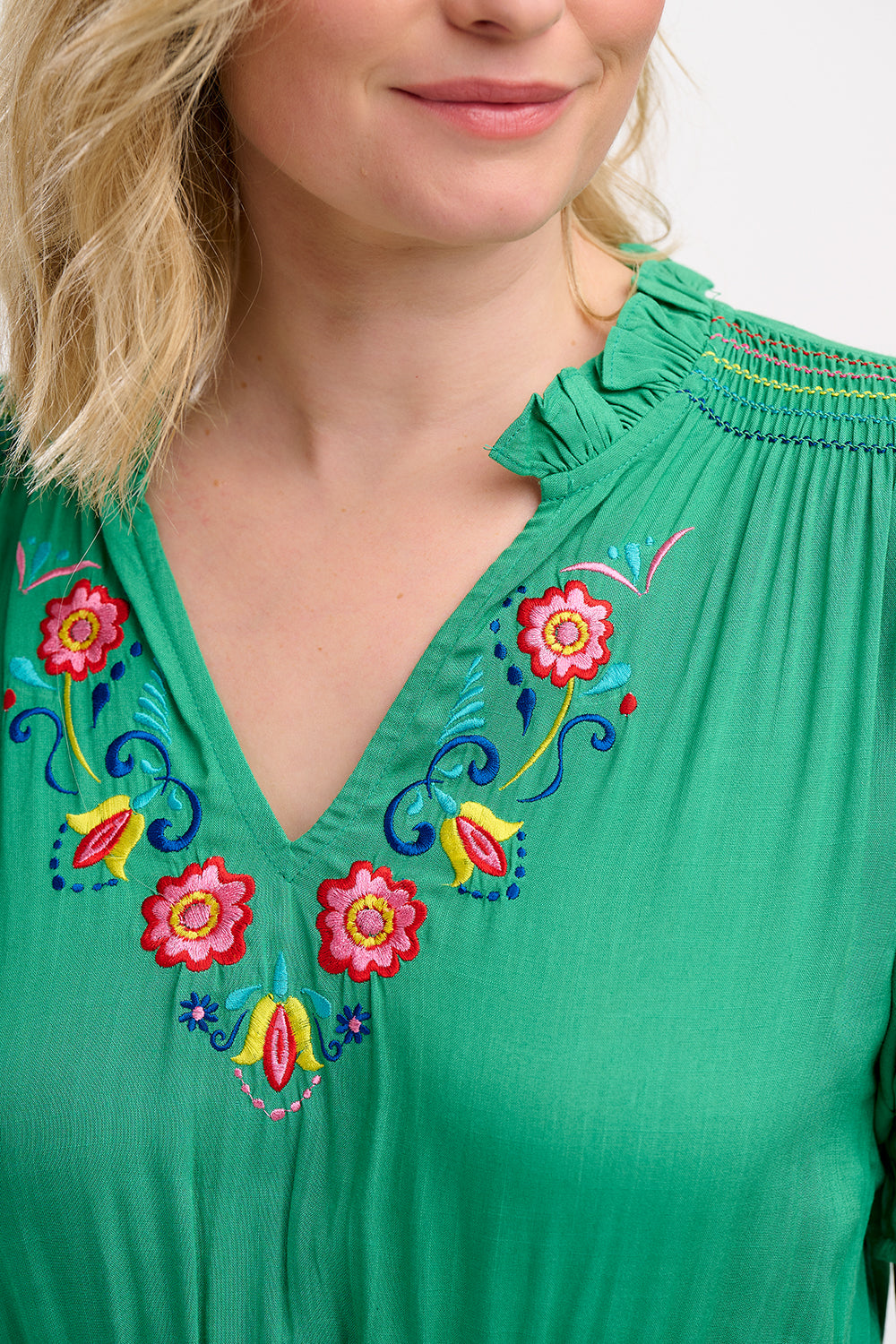 A model wearing a green midi dress with short sleeves, shirred shoulders, and floral embroidery around the neckline.