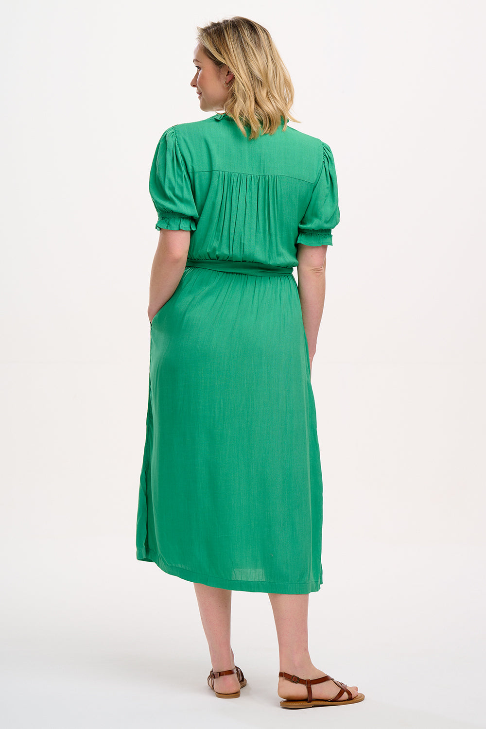 A model wearing a green midi dress with short sleeves, shirred shoulders, and floral embroidery around the neckline.