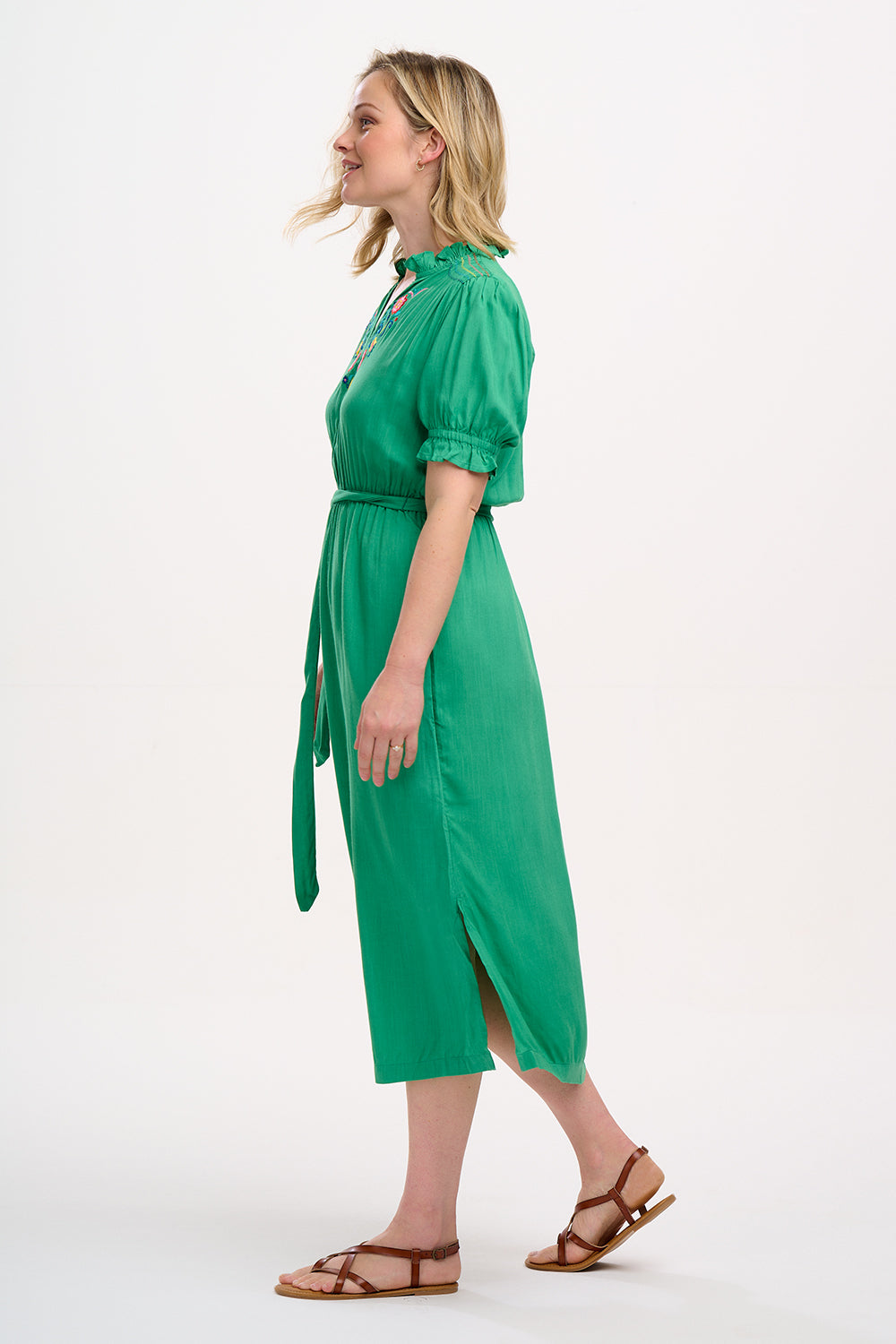 A model wearing a green midi dress with short sleeves, shirred shoulders, and floral embroidery around the neckline.