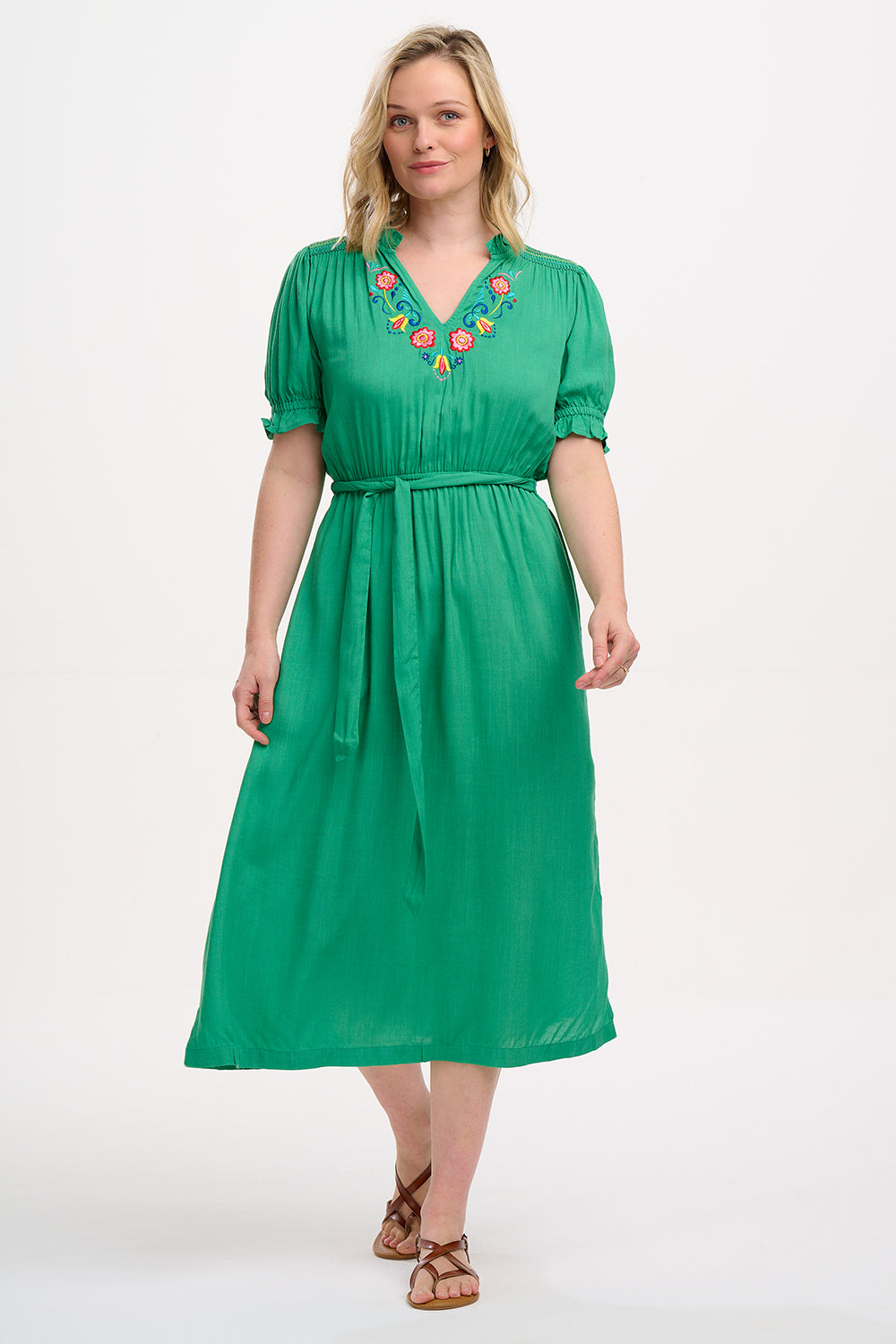A model wearing a green midi dress with short sleeves, shirred shoulders, and floral embroidery around the neckline.
