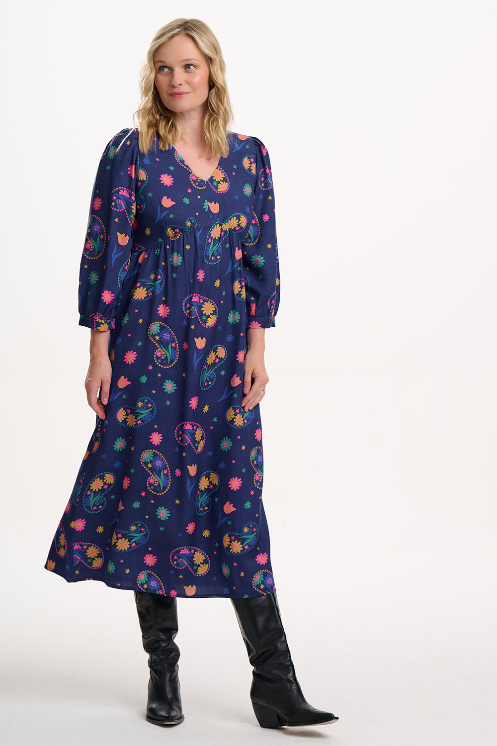 Sugarhill Brighton model wearing a long, dark blue dress with colourful floral patterns on a white background