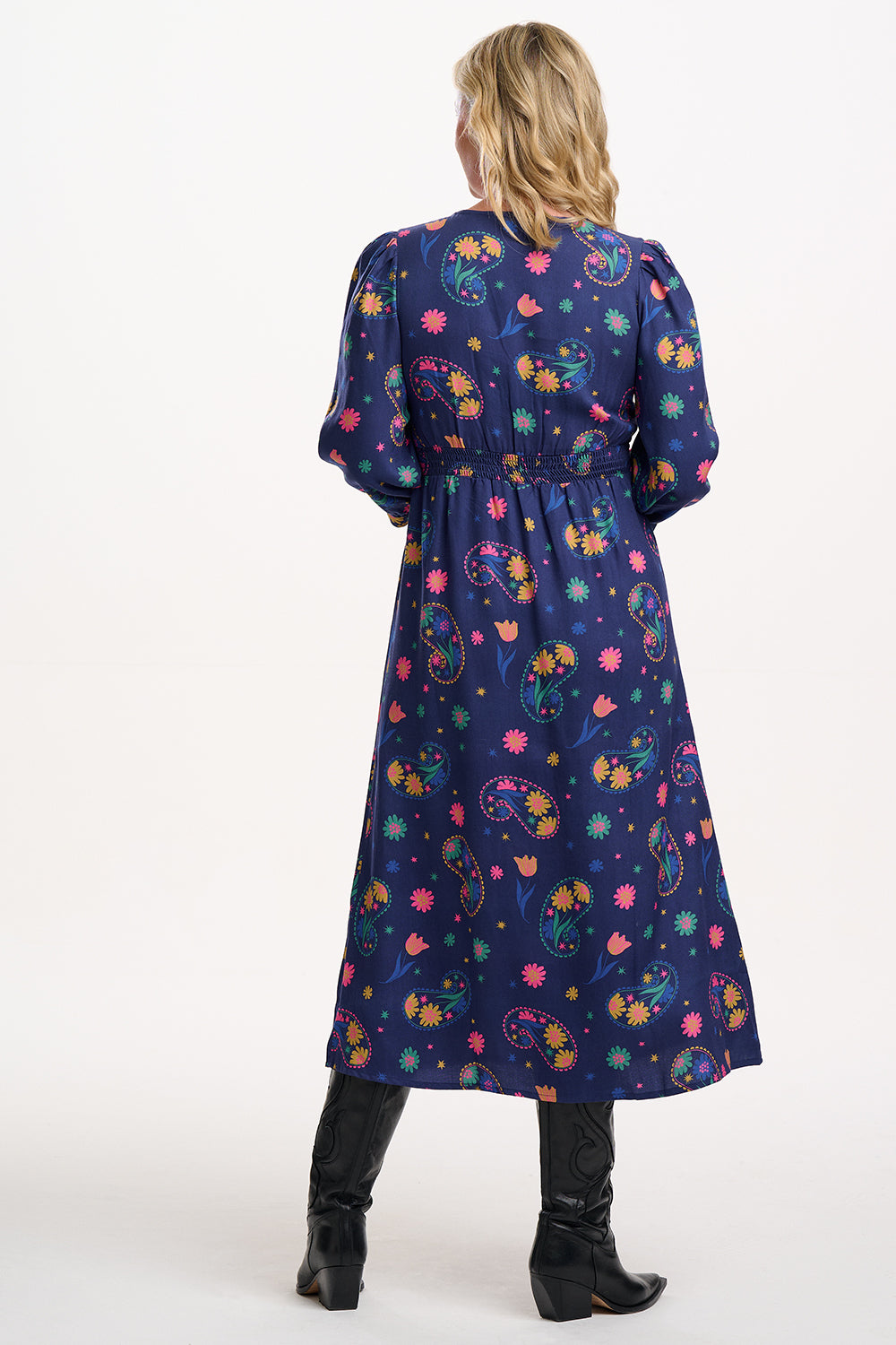 Sugarhill Brighton model wearing a long, dark blue dress with colourful floral patterns on a white background