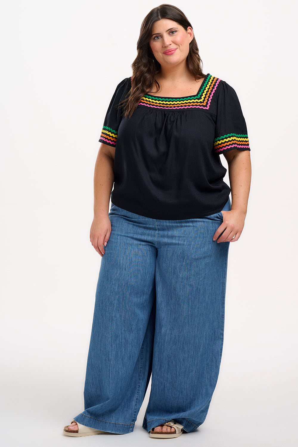 A woman wearing a black top with rainbow-colored ric rac detailing around the square neckline.