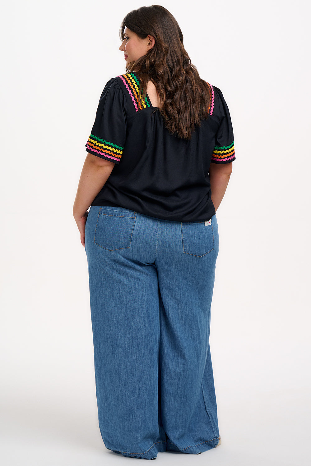 A woman wearing a black top with rainbow-colored ric rac detailing around the square neckline.