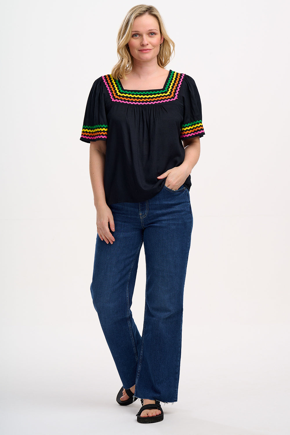 A woman wearing a black top with rainbow-colored ric rac detailing around the square neckline.