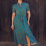 A model wearing a midi shirt dress with a green base and concentric circle pattern in blue, pink, and red. The dress features a neat collar, a button front, and puff short sleeves.