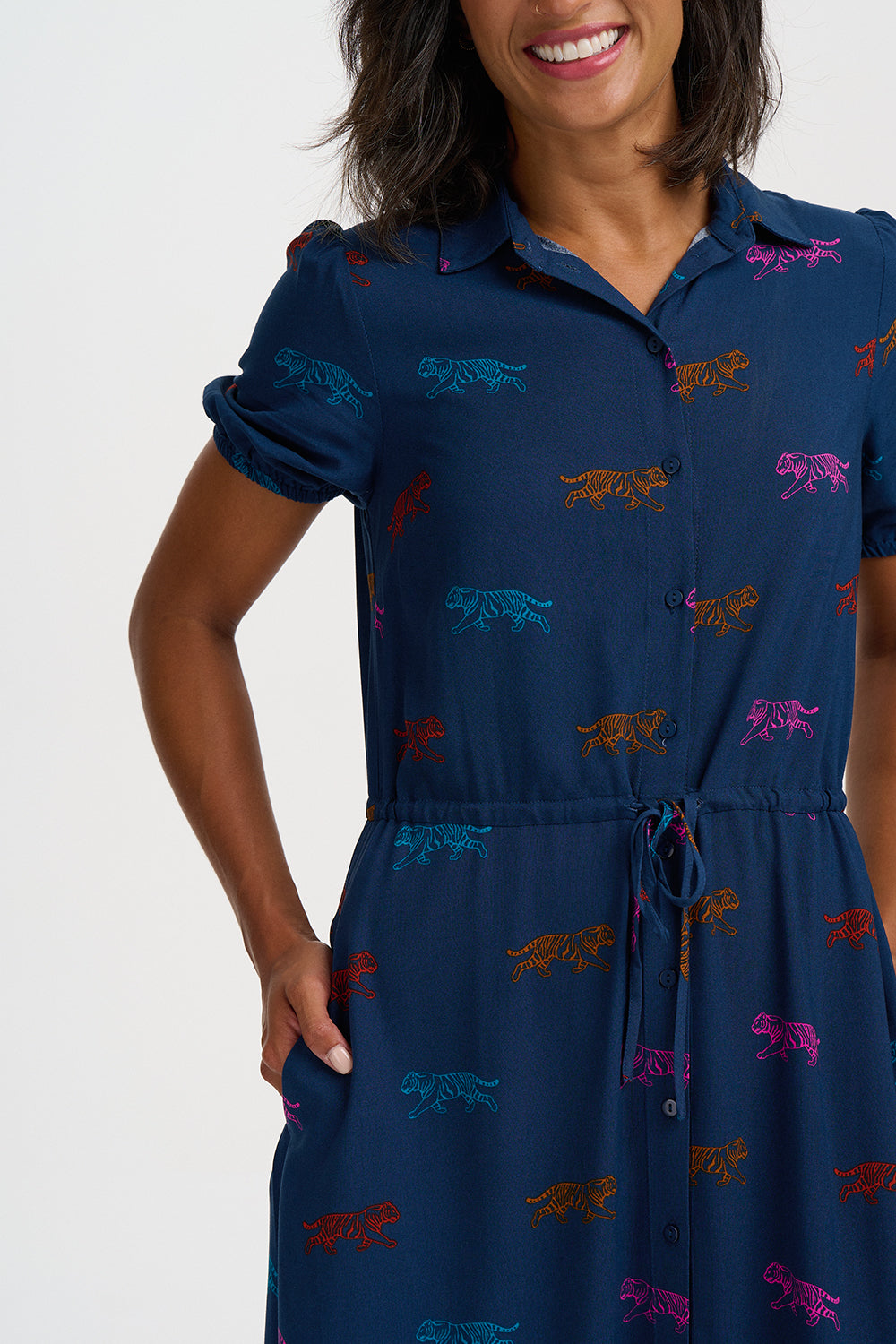A woman wearing a navy blue short-sleeve collared dress with an allover embroidered multicolor animal print, featuring a drawstring waist and button-front closure.
