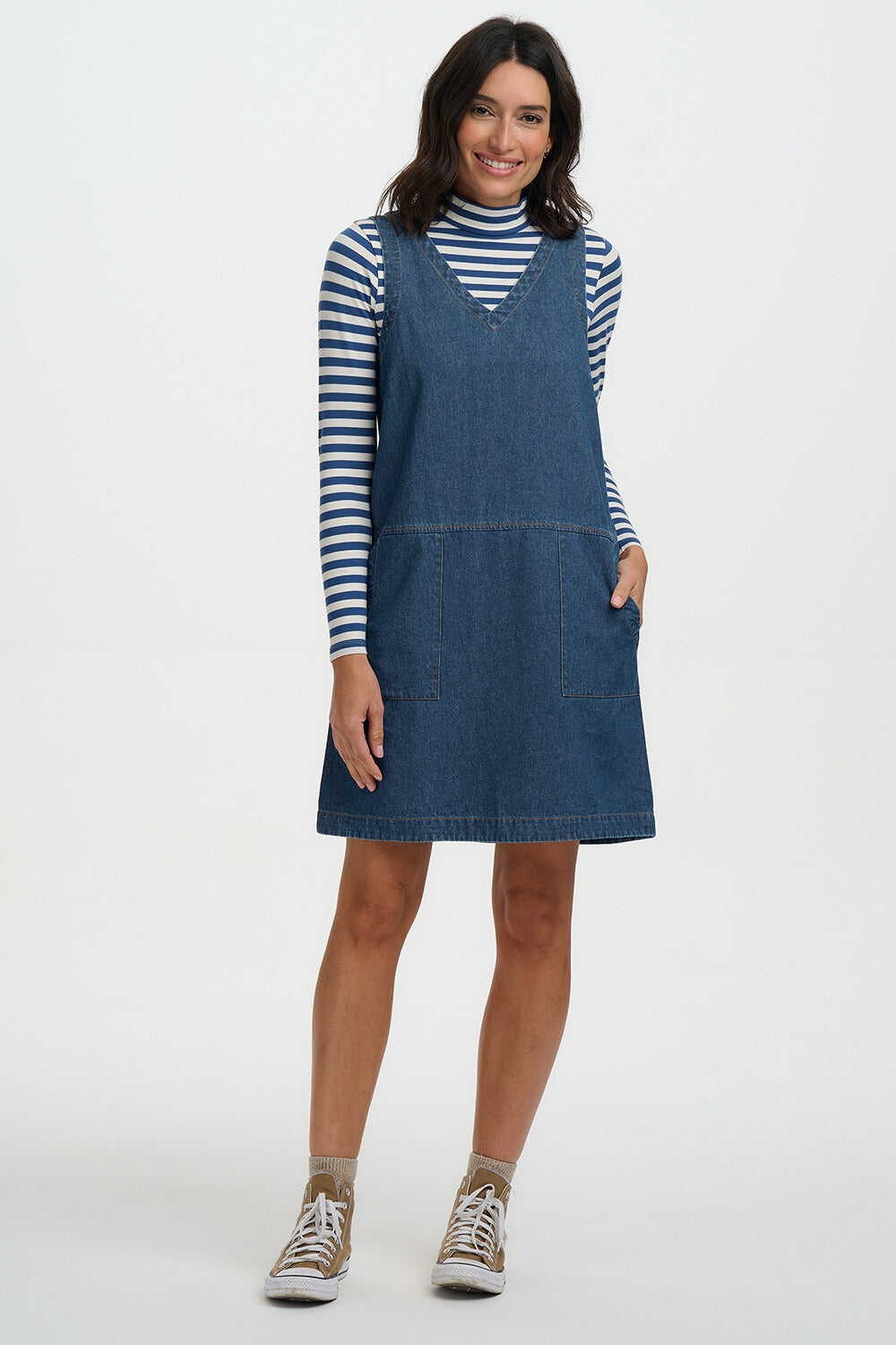 Woman wearing a blue denim dress over a striped shirt on a white background