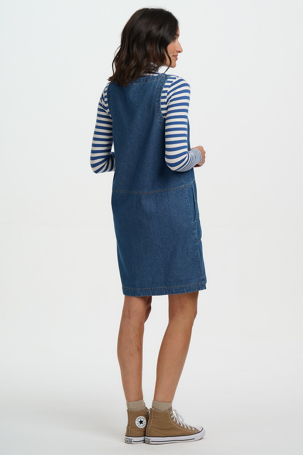 Woman wearing a blue denim dress over a striped shirt on a white background