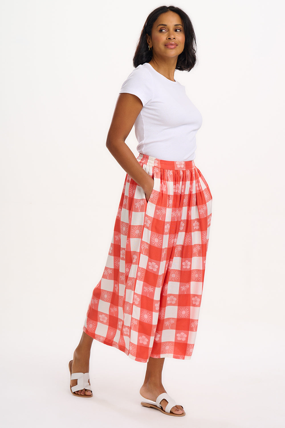 A model wearing an off-white and coral tropical gingham skirt with a fitted waistband and side pockets.
